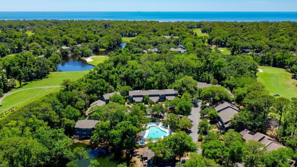 an aerial view of a resort with a pool, golf course, and surrounded by green trees